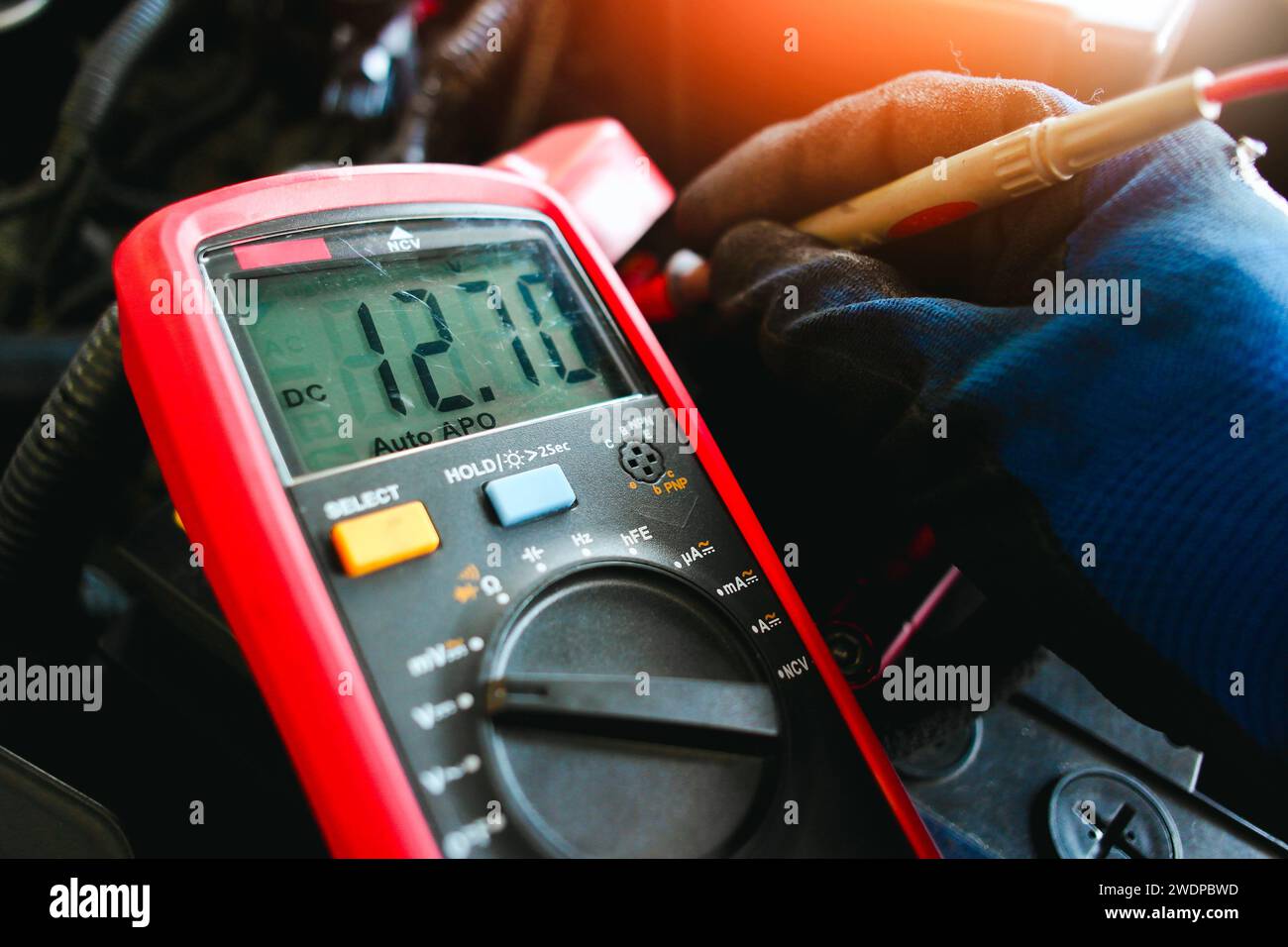 Prüfung der Fahrzeugbatteriespannung mit einem digitalen Multimeter durch den Autotechniker, Anzeige der Fahrzeugspannung auf dem schwarzen Bildschirm des Digitalmultimeters, Fahrzeugmaint Stockfoto