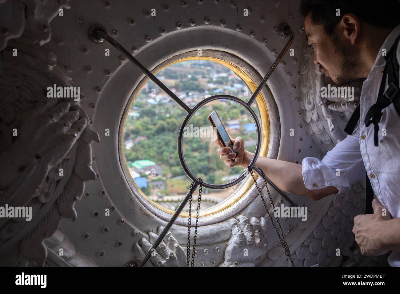 Chiang Rai, Thailand. Januar 2024. Ein Tourist macht ein Foto vom Fenster von Guanyin bindi aus der Guanyin-Statue. Der „Wat Huay Pla Kang“, auch bekannt als „großer Buddha von Chiang Rai“, ist bekannt für seine riesige weiße Statue von Guanyin (in der chinesischen Mythologie die Göttin der Barmherzigkeit). Der kürzlich erbaute Tempel ist eine Mischung aus thailändischem Lanna und chinesischem Stil und liegt auf einem Hügel im ländlichen Gebiet nördlich der Stadt Chiang Rai. Quelle: SOPA Images Limited/Alamy Live News Stockfoto