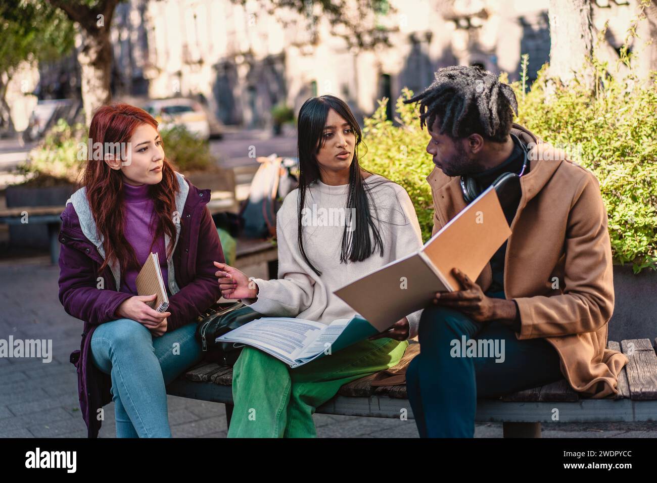 Drei verschiedene Studenten sind in einer Gruppensitzung im Freien sehr engagiert, tauschen Ideen aus und lernen gemeinsam. Stockfoto