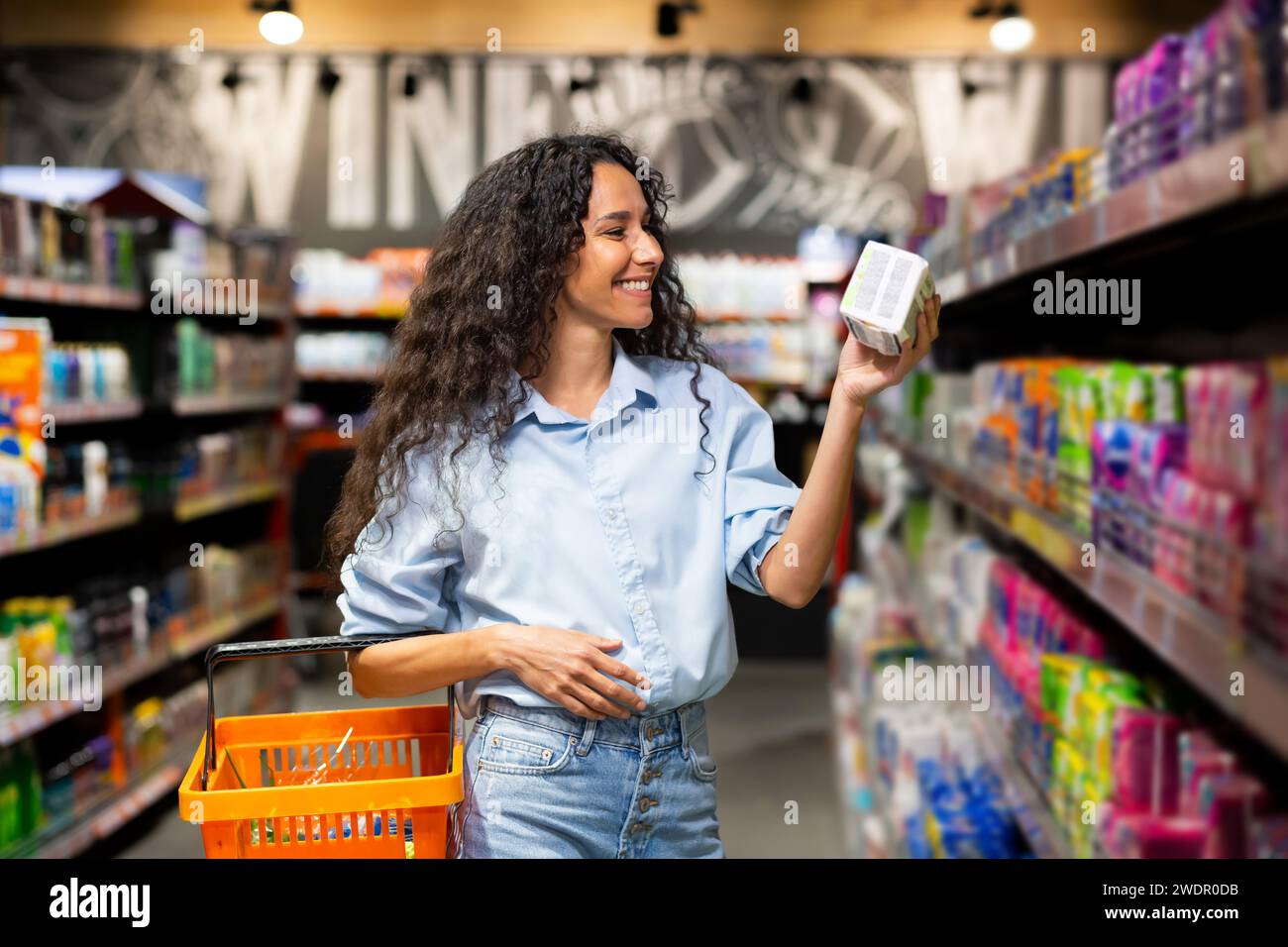 Fröhliche junge Frau mit lockigem Haar wählt Produkte im Supermarkt aus, die beispielhaft für gesunde Lebensweise und Einkaufsgewohnheiten sind. Stockfoto