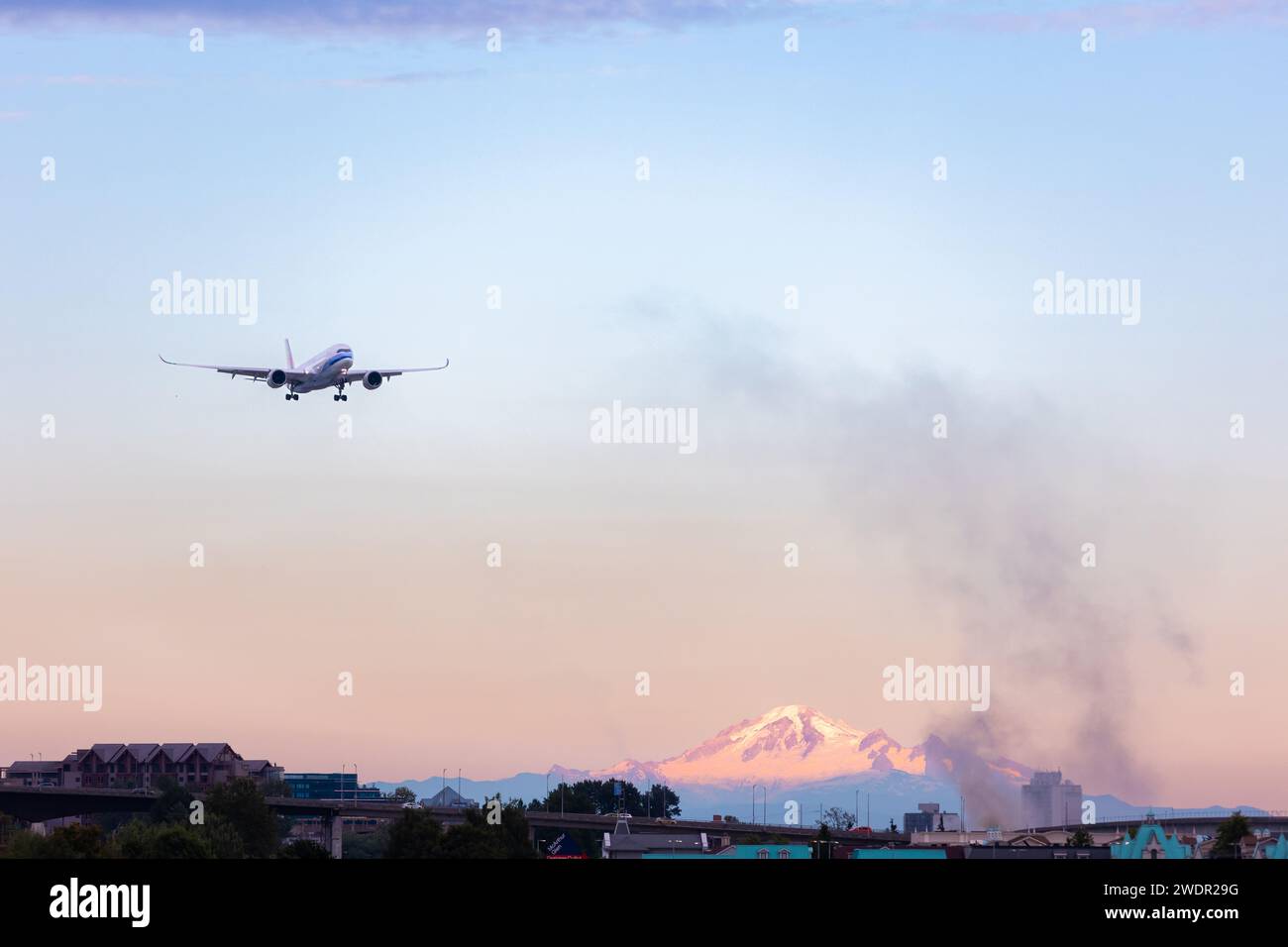 VANCOUVER, BC, KANADA - 27. JULI 2023: Boeing 777 mit Feuer in der Nähe von YVR in Richmond, BC, mit Mount Baker im Hintergrund, schwarzer Rauch, schwelend Stockfoto