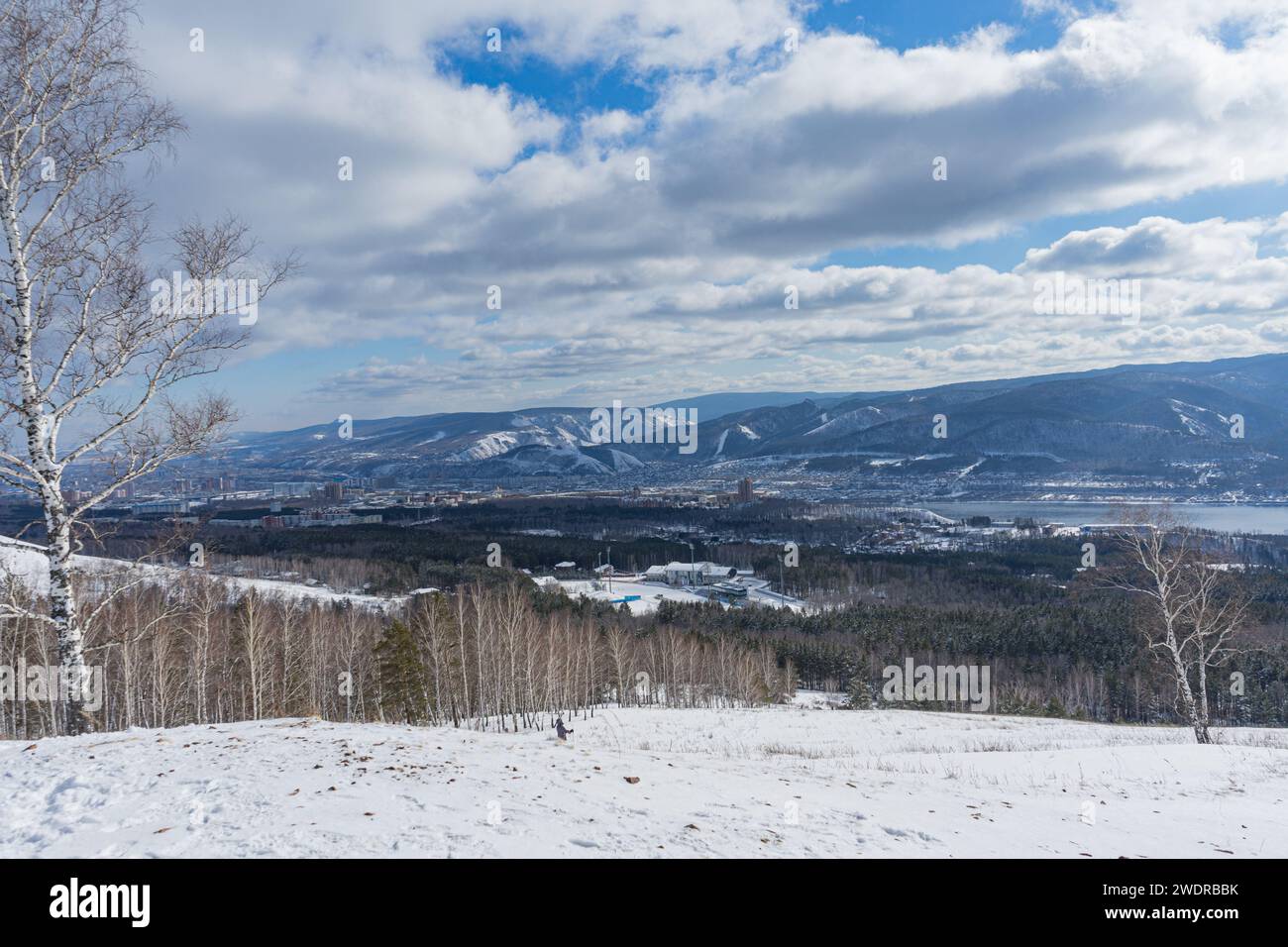 Stadtviertel und Natur. Winterlandschaft. Blauer Himmel mit niedrigen weißen Wolken über der Stadt. Gremyachaya Griva Park, Krasnojarsk, Russland. Stockfoto