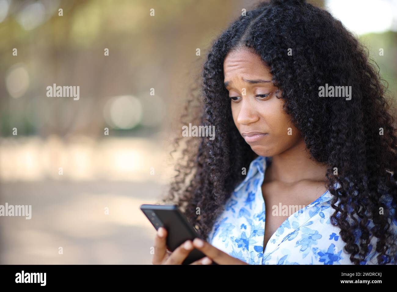 Enttäuschte schwarze Frau, die ihr Handy in einem Park überprüft Stockfoto
