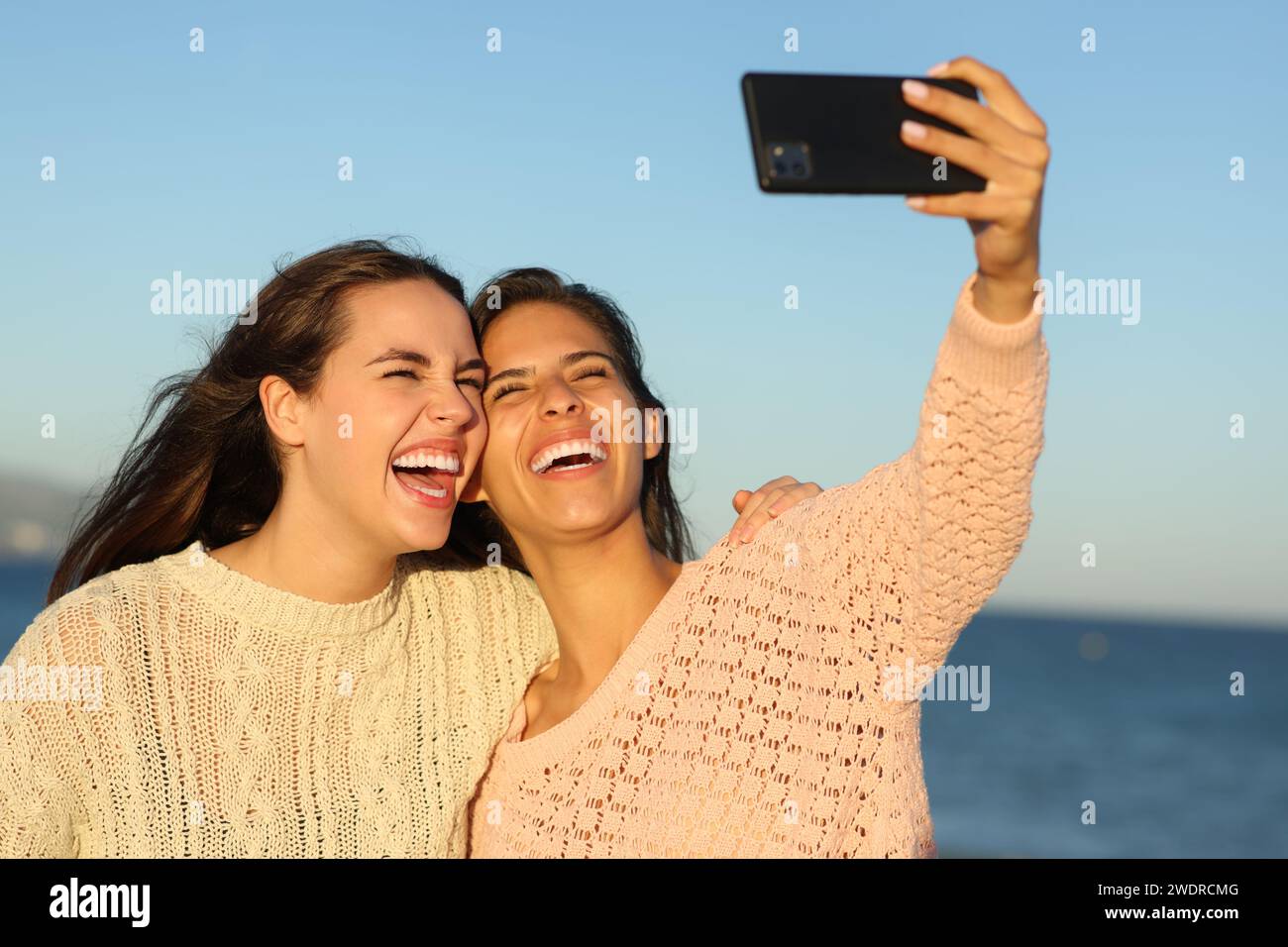 Zwei glückliche Freunde, die Selfies machen, lachen am Strand bei Sonnenuntergang Stockfoto