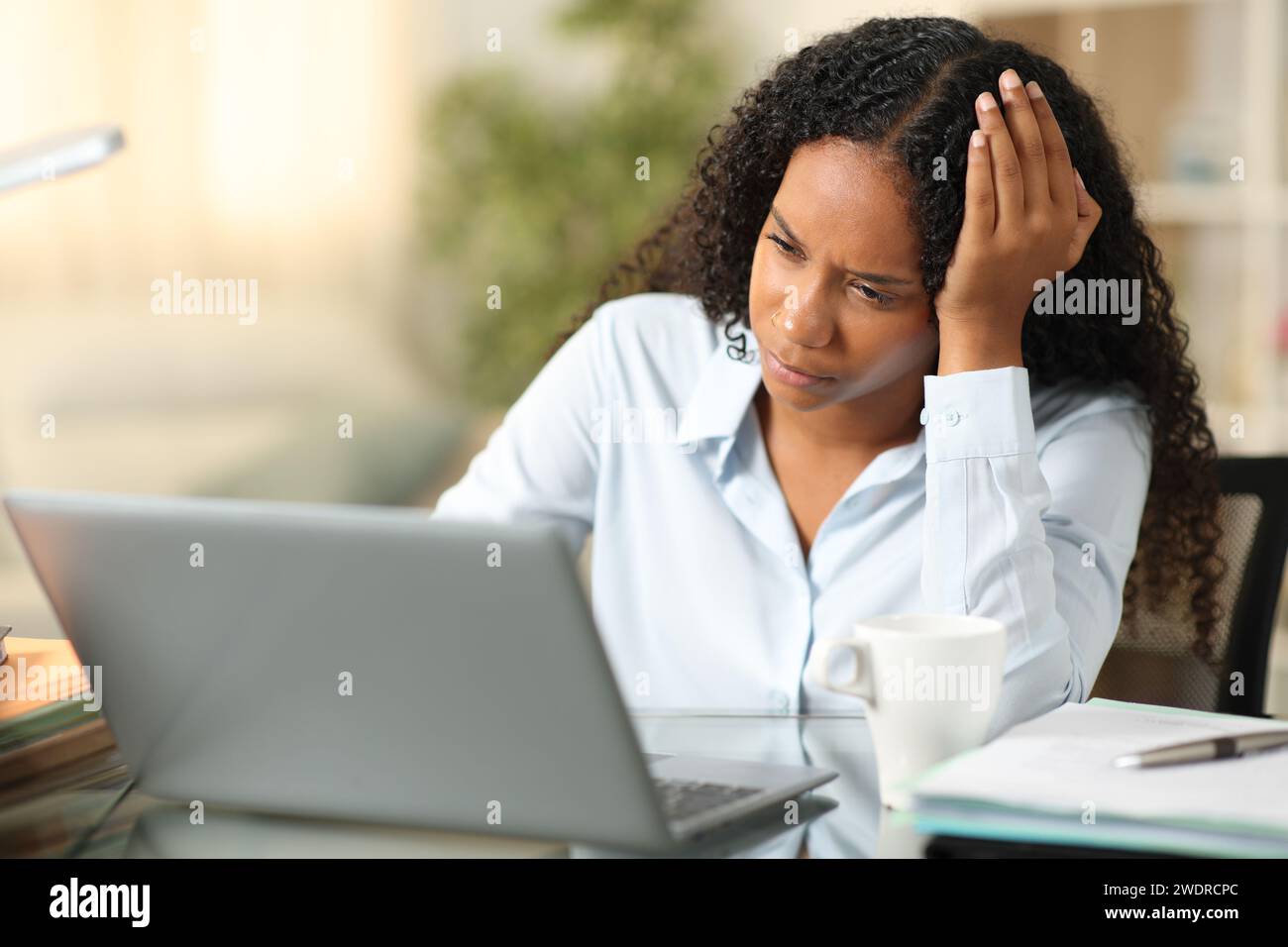 Besorgter schwarzer Telearbeiter, der den Laptop überprüft, der zu Hause arbeitet Stockfoto