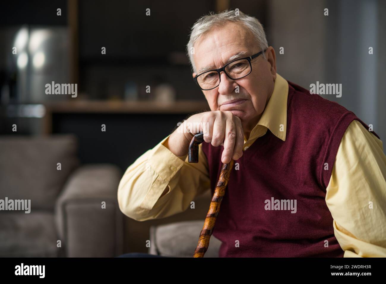 Ein nachdenklicher und besorgter Seniorenmann sitzt in seinem Haus auf dem Bett. Porträt eines Seniorenmannes mit Gehstock. Stockfoto