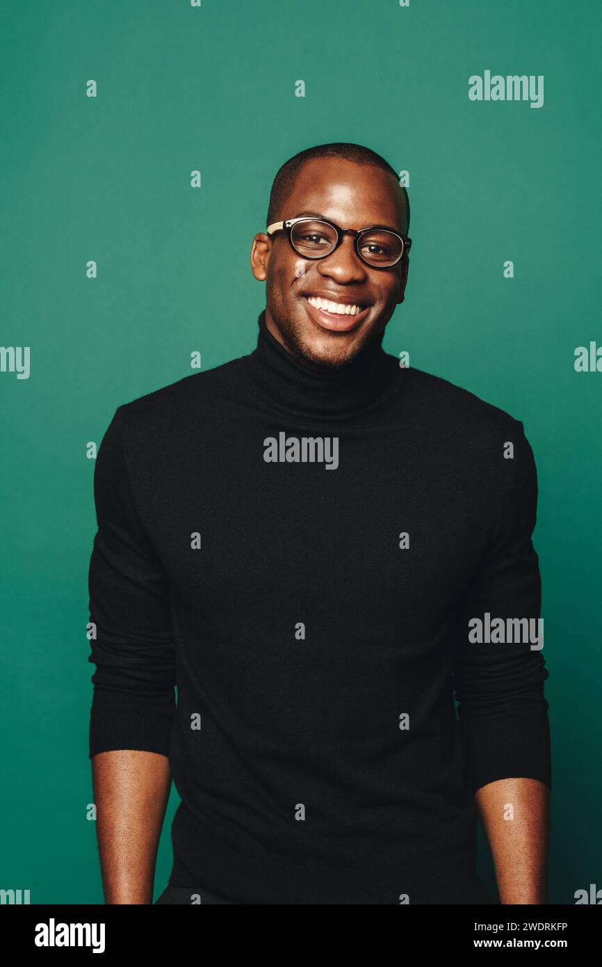 Porträt eines glücklichen schwarzen Mannes, der legere Kleidung trägt und vor grünem Hintergrund steht. Er trägt eine stilvolle Brille und einen eleganten Pullover Stockfoto