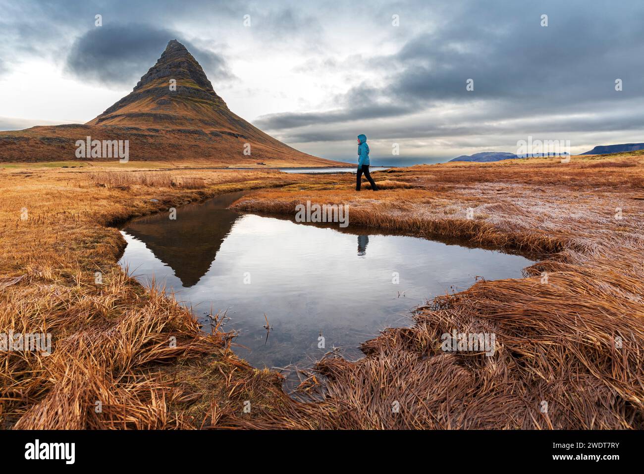 Frau spaziert vor dem berühmten Kirkjufell-Berg, der sich im Wasser eines kleinen Sees, der Halbinsel Snaefellsnes, spiegelt Stockfoto