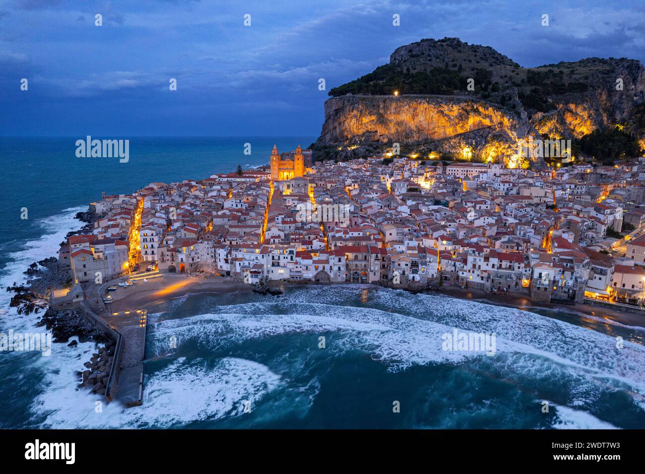 Das beleuchtete Fischerdorf Cefalu mit dem Felsen auf der Spitze der Altstadt von der Drohne in der Abenddämmerung aus gesehen, Cefalu, Provinz Palermo Stockfoto