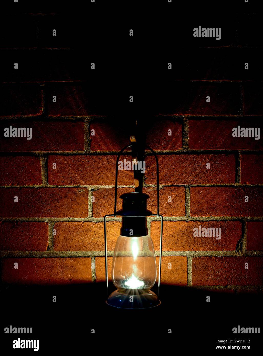 Eine Teelicht-Laterne, die nachts an einer Wand hängt und Licht und Schatten auf das Mauerwerk wirft. Stockfoto