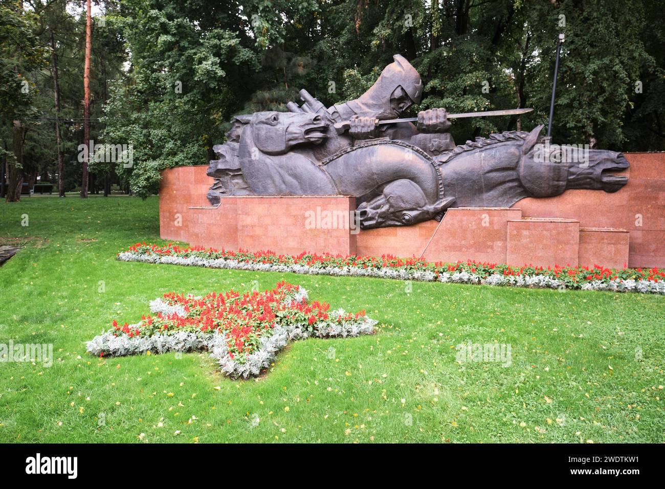 Links befindet sich der Teil der Gedenkstätte mit einem „Eid“-Thema, ein Soldat führt Pferde. Am Denkmal des Ruhms im Panfilov Park in Almaty, Kasachstan. Stockfoto
