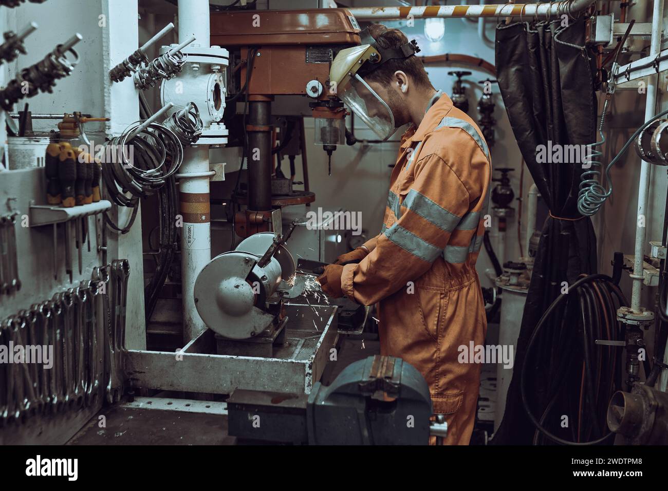 Maschinenbauingenieur, der in der Werkstatt an Schleifmaschinen arbeitet, mit Gesichtsschutz, Overall und Handschuhen. Stockfoto