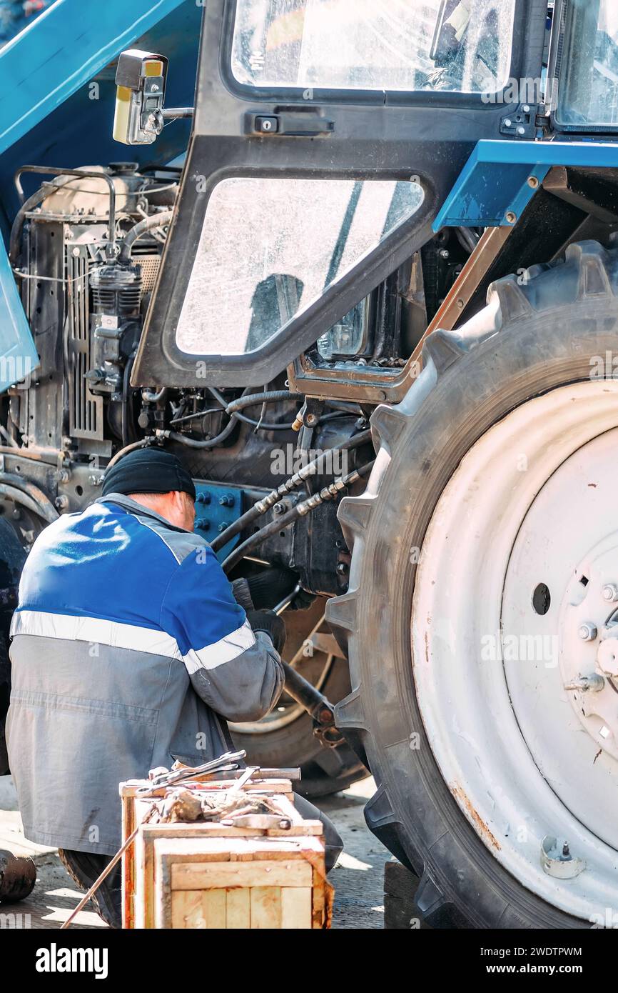 Der Mechaniker repariert den Motor des Traktors oder schwerer Ausrüstung. Landwirt inspiziert und diagnostiziert Landmaschinen. Stockfoto