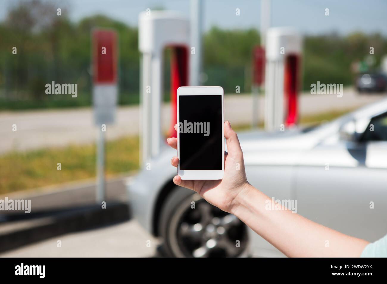 Hand mit Telefon auf einem Hintergrund einer Ladestation für Elektroautos. Stockfoto