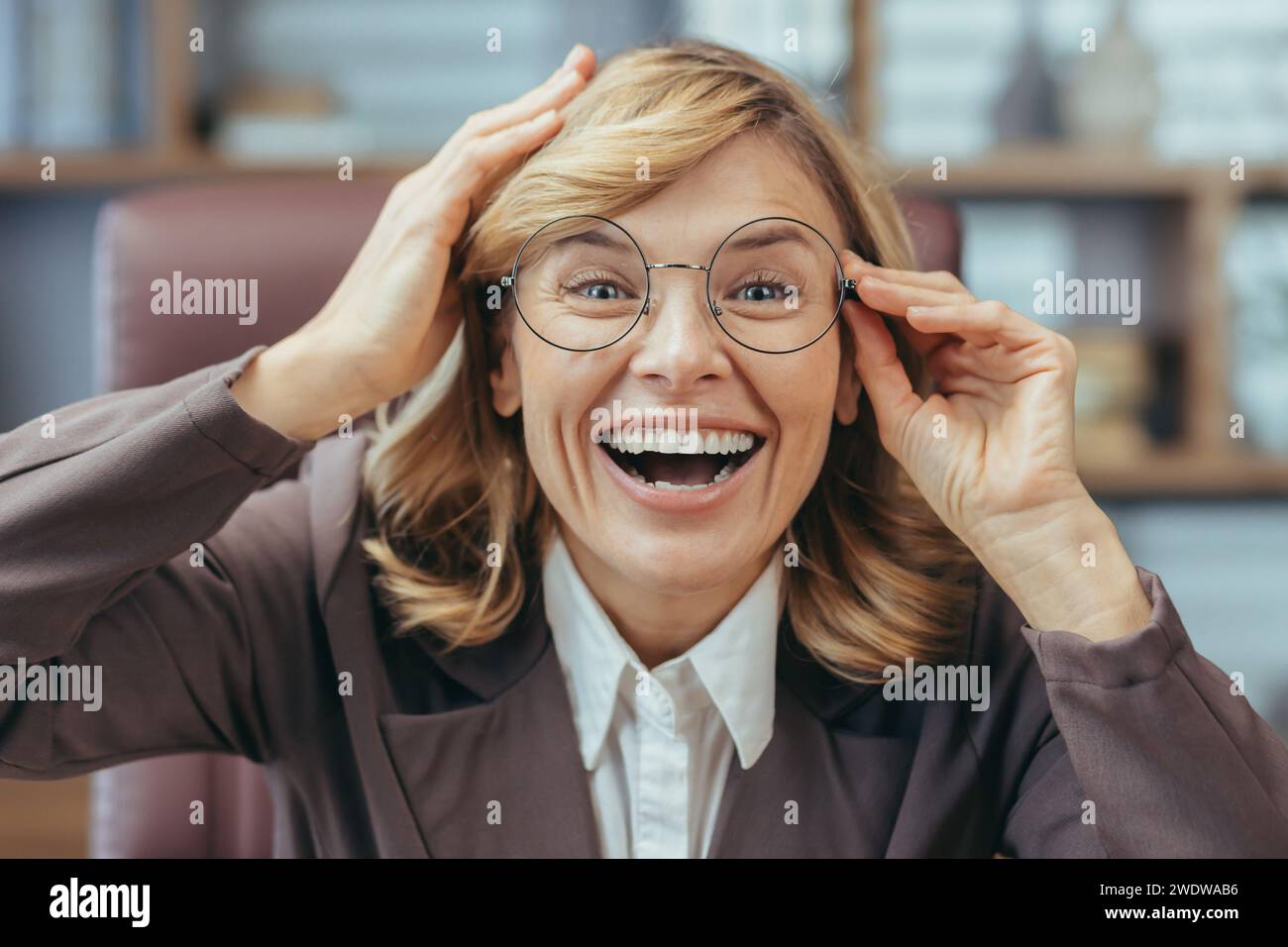 Fröhliche, reife Geschäftsfrau, die von zu Hause aus arbeitet und in einer stilvollen Einrichtung lacht. Remote Senior Professional mit Brille. Stockfoto