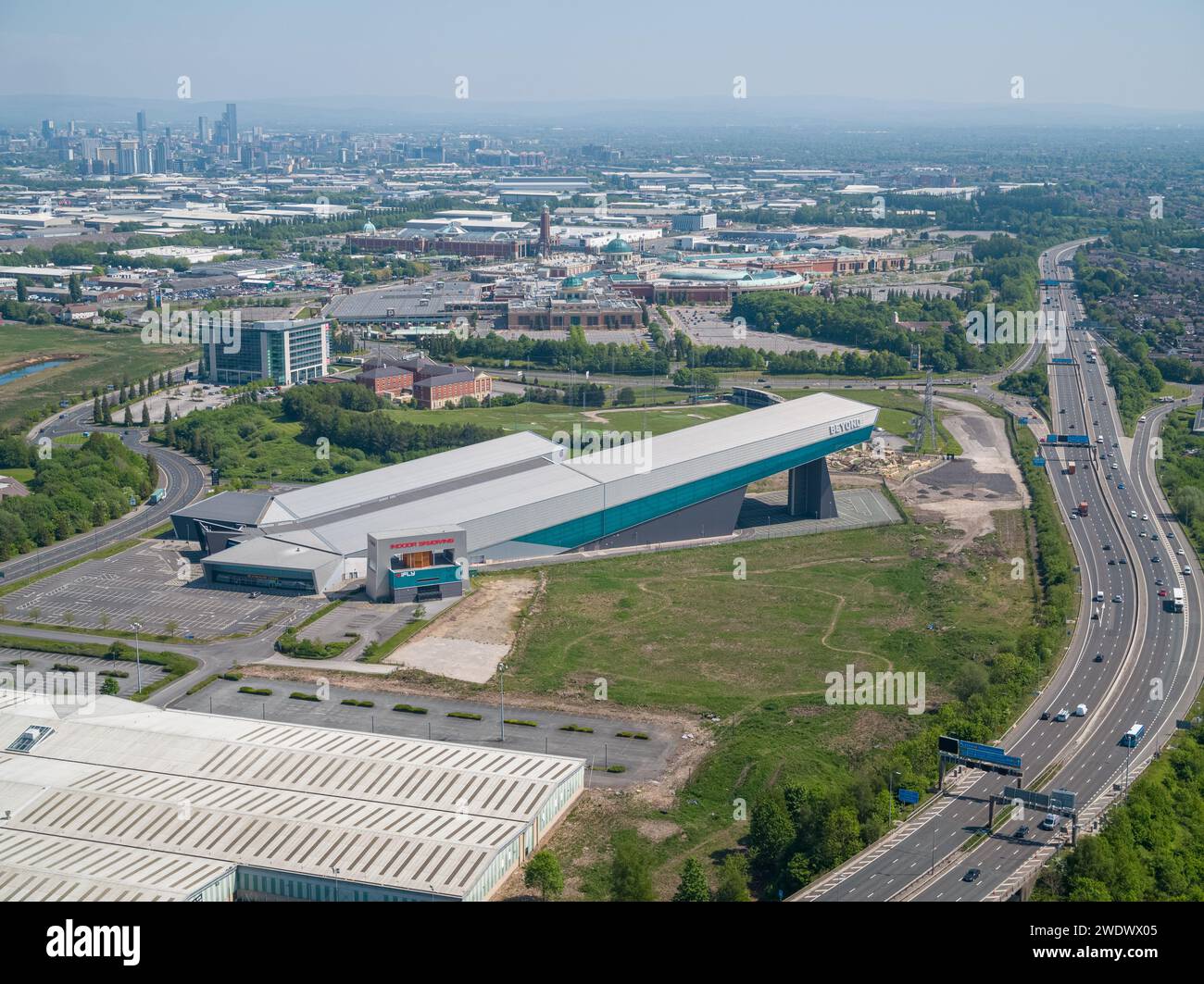 Luftaufnahme der Hallen-Skipiste von Chill Factore am Beyond, Autobahn M60 mit dem Trafford Centre & Manchester City Centre in der Ferne Stockfoto
