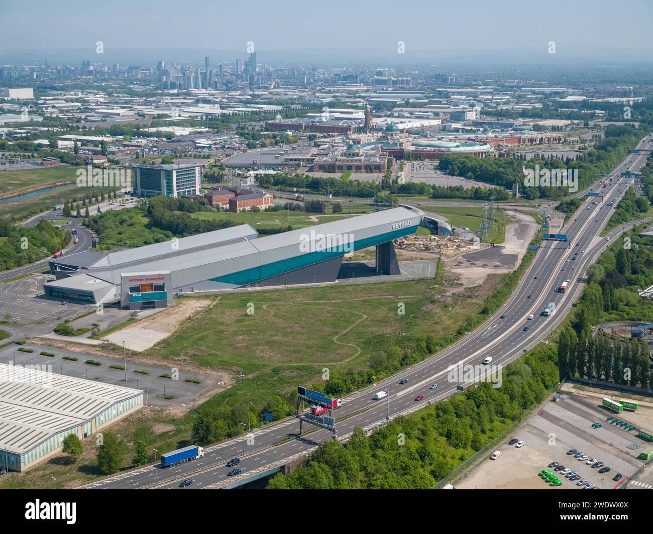 Luftaufnahme der Hallen-Skipiste von Chill Factore am Beyond, Autobahn M60 mit dem Trafford Centre & Manchester City Centre in der Ferne Stockfoto