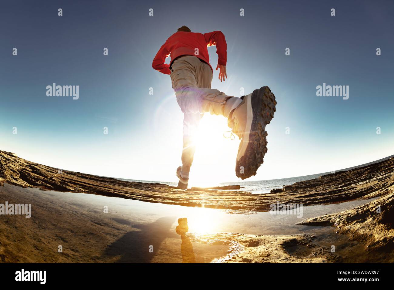 Sportlicher Athlet läuft und springt bei Sonnenuntergang über Pfützen. Nahaufnahme des Sportlers Bein und Schuh Stockfoto