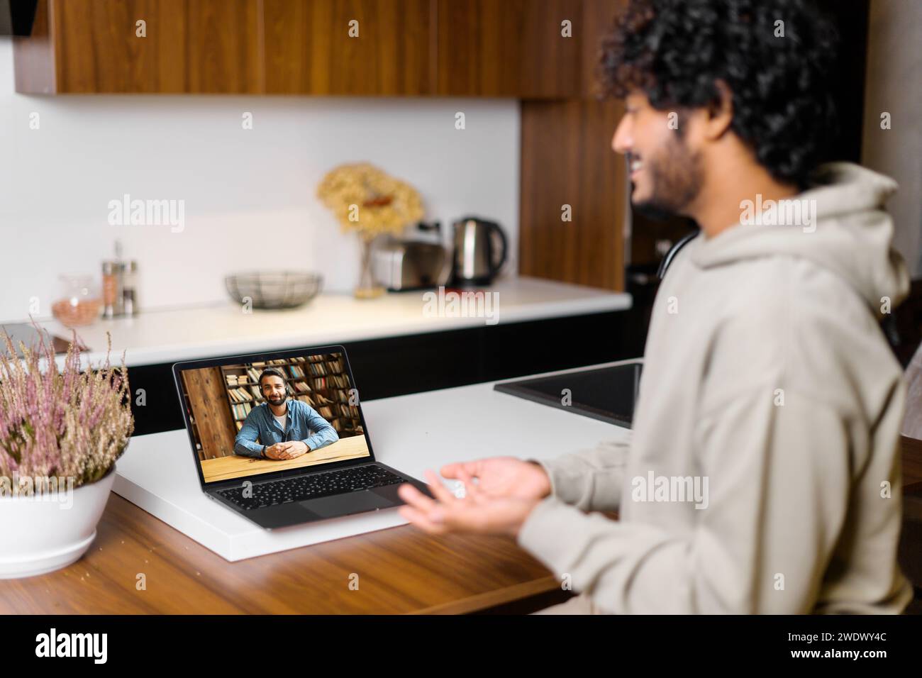 Curly Indian man führt ein persönliches Videogespräch, spricht mit einem Kollegen oder Kunden und betont die persönliche Verbindung in der digitalen Kommunikation Stockfoto