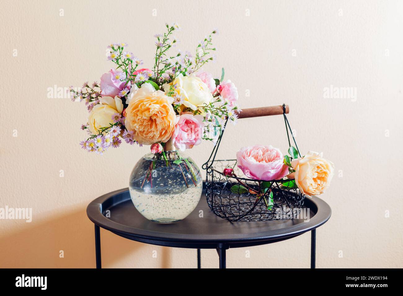 Frisches Bouquet von Rosenblüten in Glasvase auf den Tisch gelegt. Nahaufnahme von rosa gelben Blüten mit Korb. Einrichtung im Sommer Stockfoto