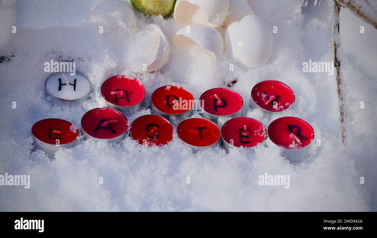 Frohe Ostern steht auf roten Teelichtern, die im Schnee liegen. Stockfoto