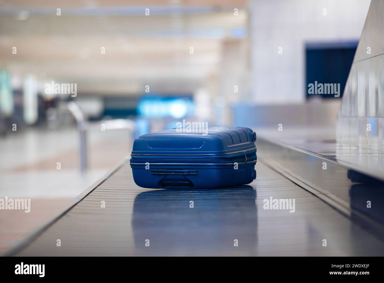 Reisen mit dem Flugzeug. Selektiver Fokus auf einsamen blauen Koffern bei der Gepäckausgabe im Flughafenterminal. Stockfoto