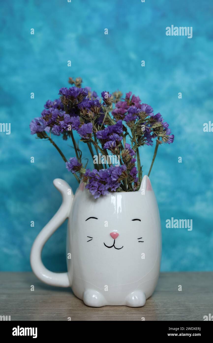 Ein Strauß getrockneter Blumen in einer weißen Katzenvase auf blauem Hintergrund Stockfoto