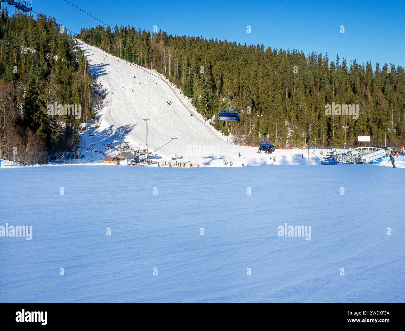 Steile Skipiste, Sessellifte, Skifahrer und Snowboarder im Skigebiet Bialka Tatrzanska in Polen im Winter bei tiefem Dezemberlicht. Großer Kopierbereich im Stockfoto