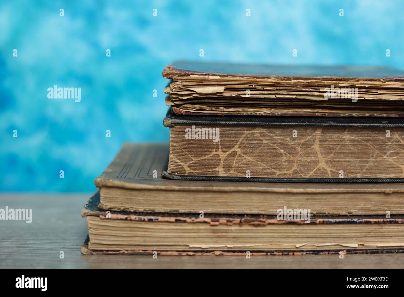 Stapel alter Bücher auf einem Holztisch mit blauem Hintergrund. Stockfoto