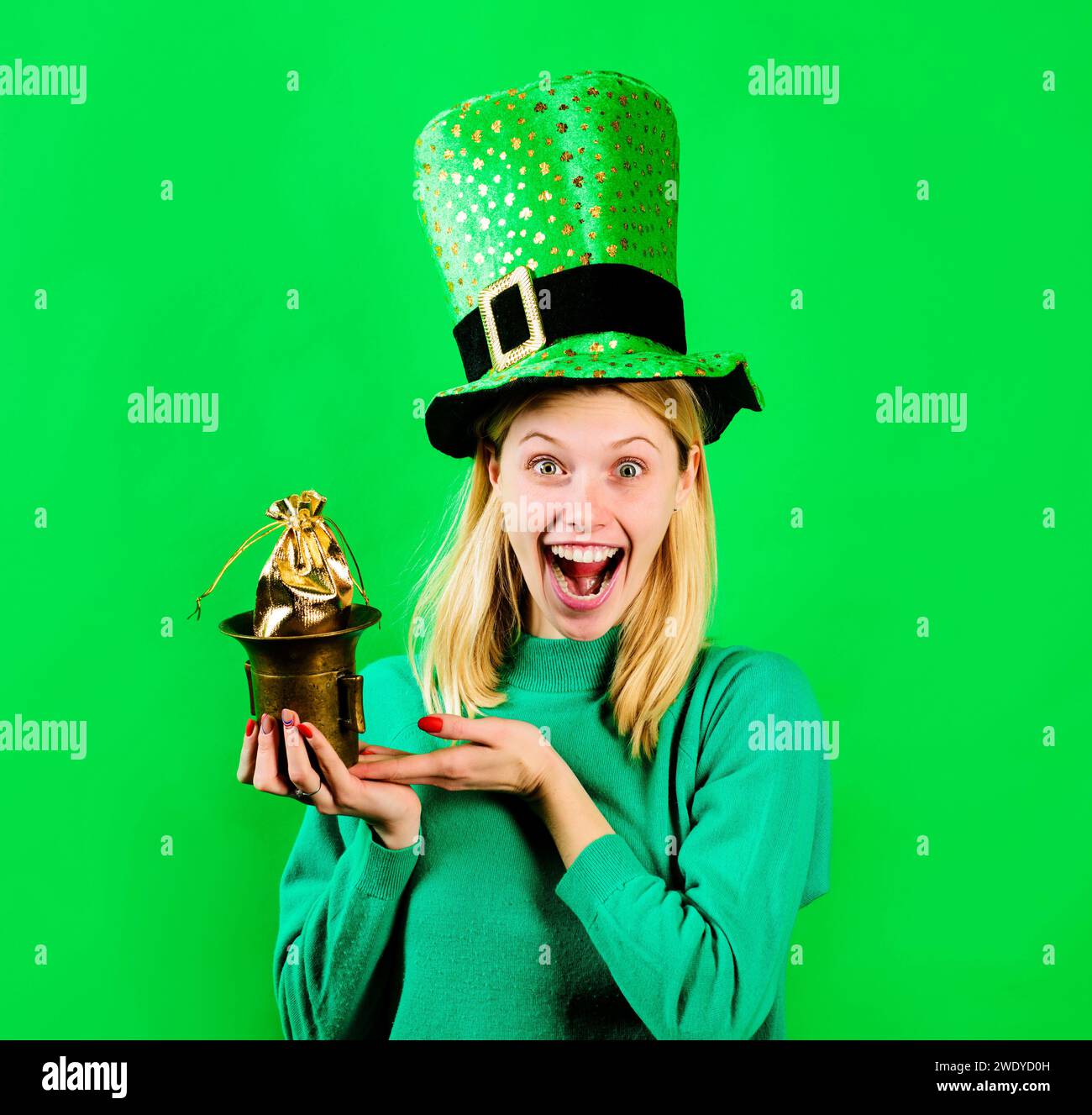 Pot Geld für Patricks Party. Glückliche Frau in grünem Hut mit einer kleinen Tasche Gold. Patricks-Feiertag. Lächelndes Mädchen in grünem Pullover und Stockfoto