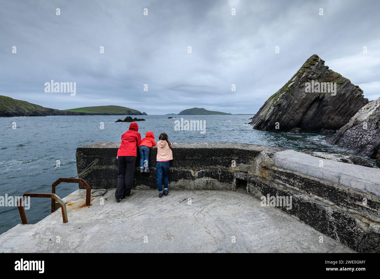 Zwei Mädchen und ein Kind schauen aus einem Aussichtspunkt am Ufer des Dingle Ring mit einer spektakulären Meereslandschaft an einem regnerischen Tag, Kerry, Irland Stockfoto