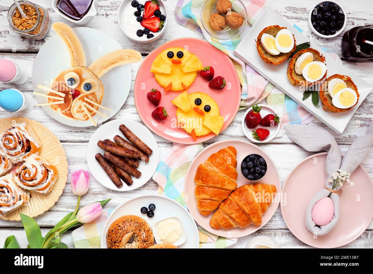 Osterfrühstück oder Brunch-Tisch. Draufsicht auf weißem Holzhintergrund. Hasenpfannkuchen, Eiernester, Hühnerfrüchte und eine Sammlung von Frühlingsnahrungsmitteln Stockfoto