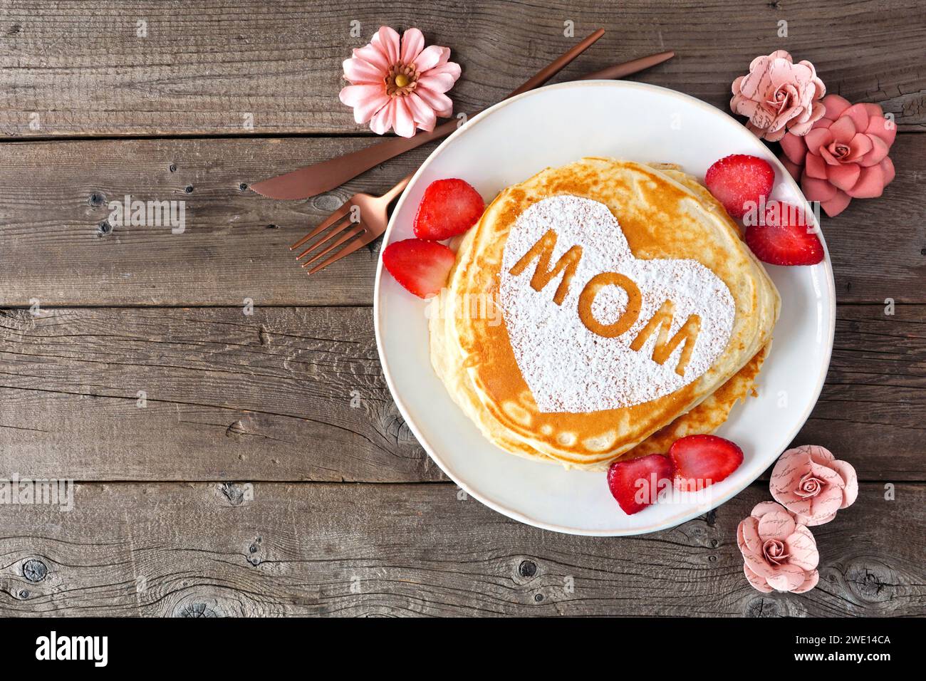 Pfannkuchen mit Herzform und MAMA-Buchstaben. Frühstückskonzept zum Muttertag. Blick von oben auf einem rustikalen Holzhintergrund. Stockfoto