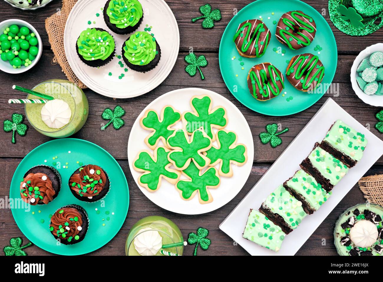 Desserts zum St. Patricks Day. Tischszene auf dunklem Holzhintergrund. Shamrock-Kekse, grüne Cupcakes, Brownies, Donuts und Süßigkeiten. Ansicht oben. Stockfoto