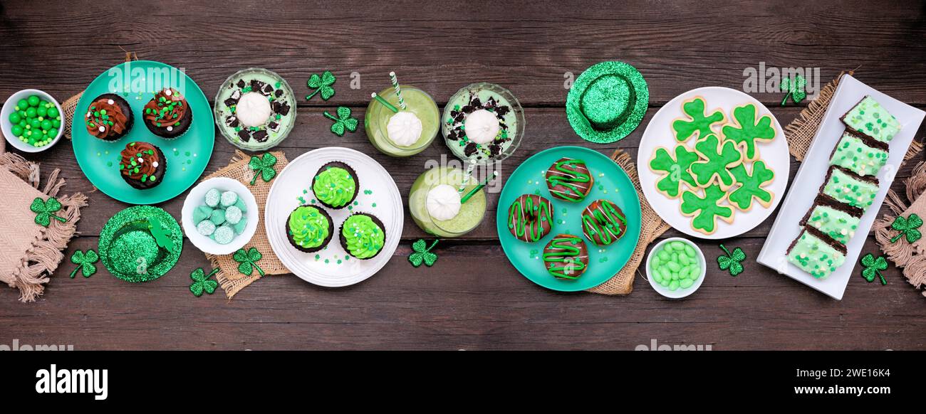 Desserts zum St. Patricks Day. Tischszene über dunklem Holzbannerhintergrund. Shamrock-Kekse, grüne Cupcakes, Brownies, Donuts und Süßigkeiten. Top dow Stockfoto