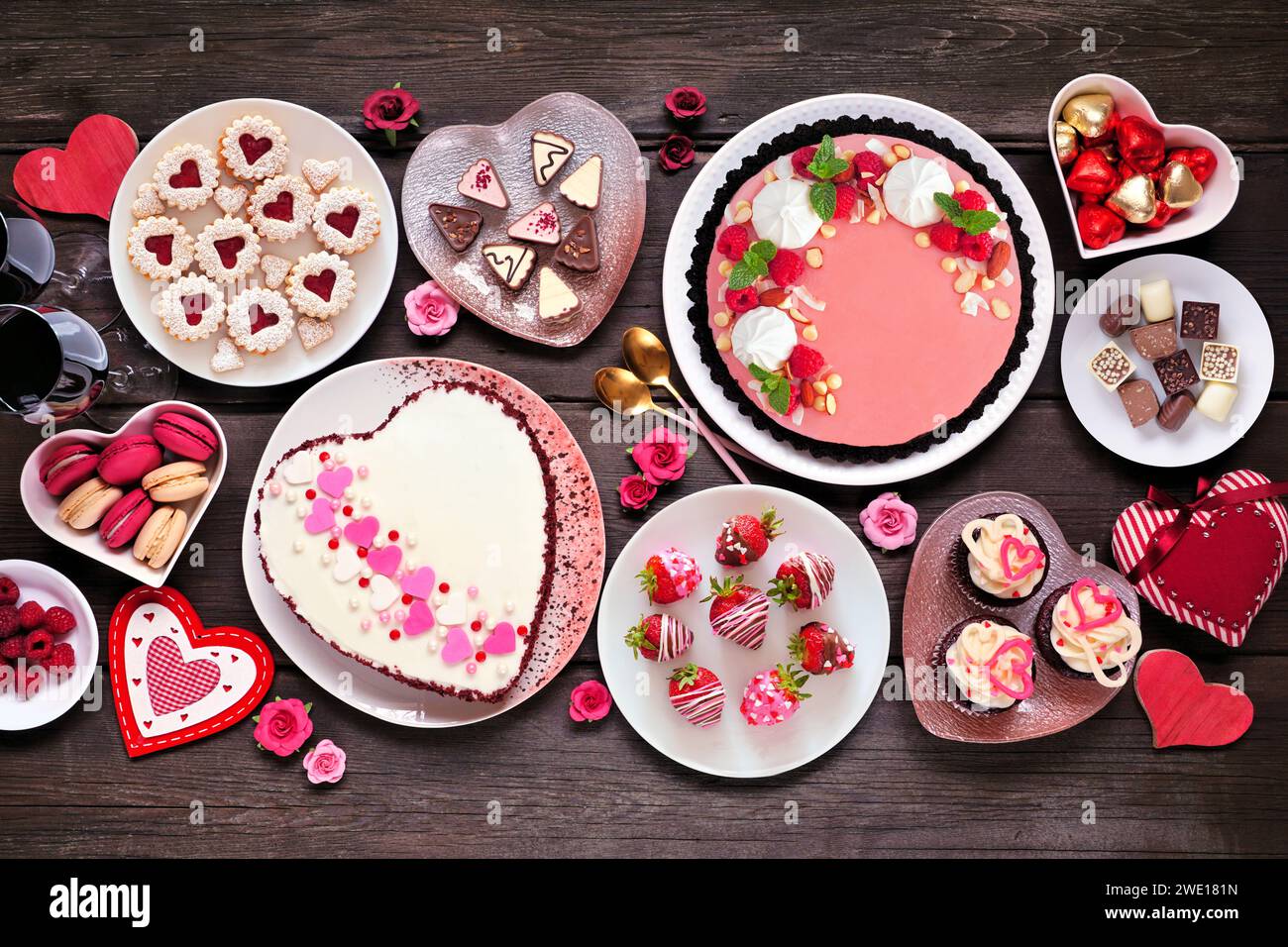 Valentinstag-Tischszene mit einer Auswahl an Desserts und Süßigkeiten. Blick von oben auf dunklem Holzhintergrund. Das Thema Liebe und Herzen. Stockfoto