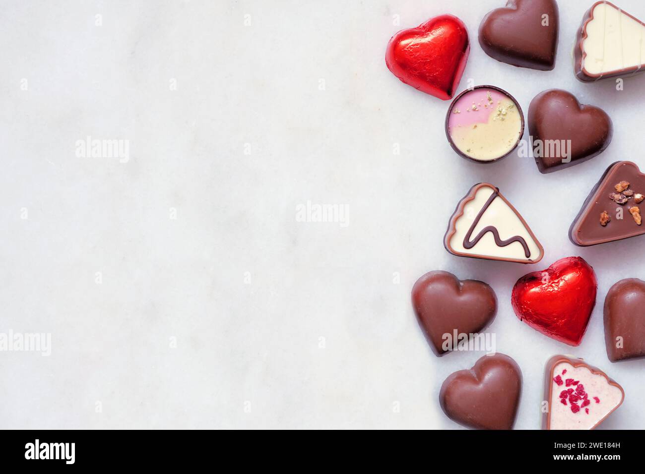 Am Valentinstag mit Schokoladenrand. Rotes und rosafarbenes Herzmotiv. Ansicht von oben nach unten auf weißem Marmorhintergrund mit Kopierraum. Stockfoto