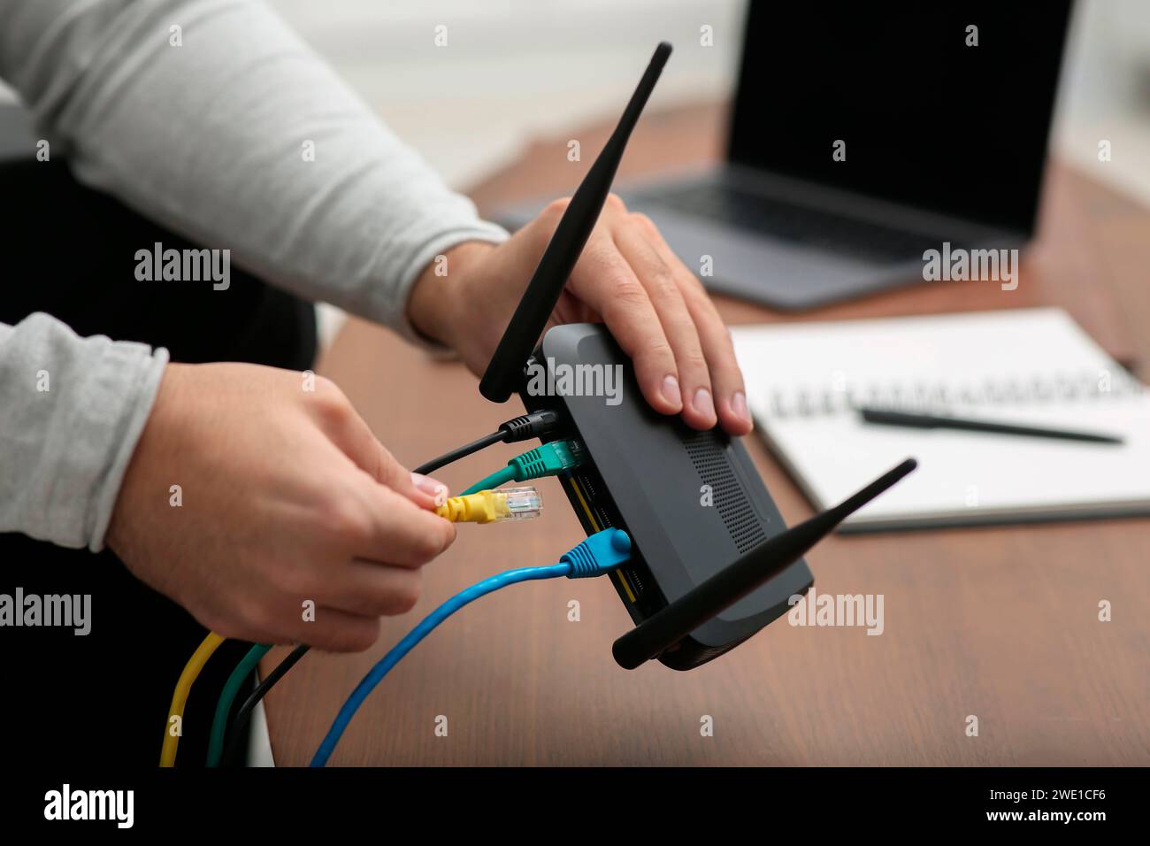 Mann, der Kabel in den WLAN-Router an einem Holztisch drinnen steckt, Nahaufnahme Stockfoto