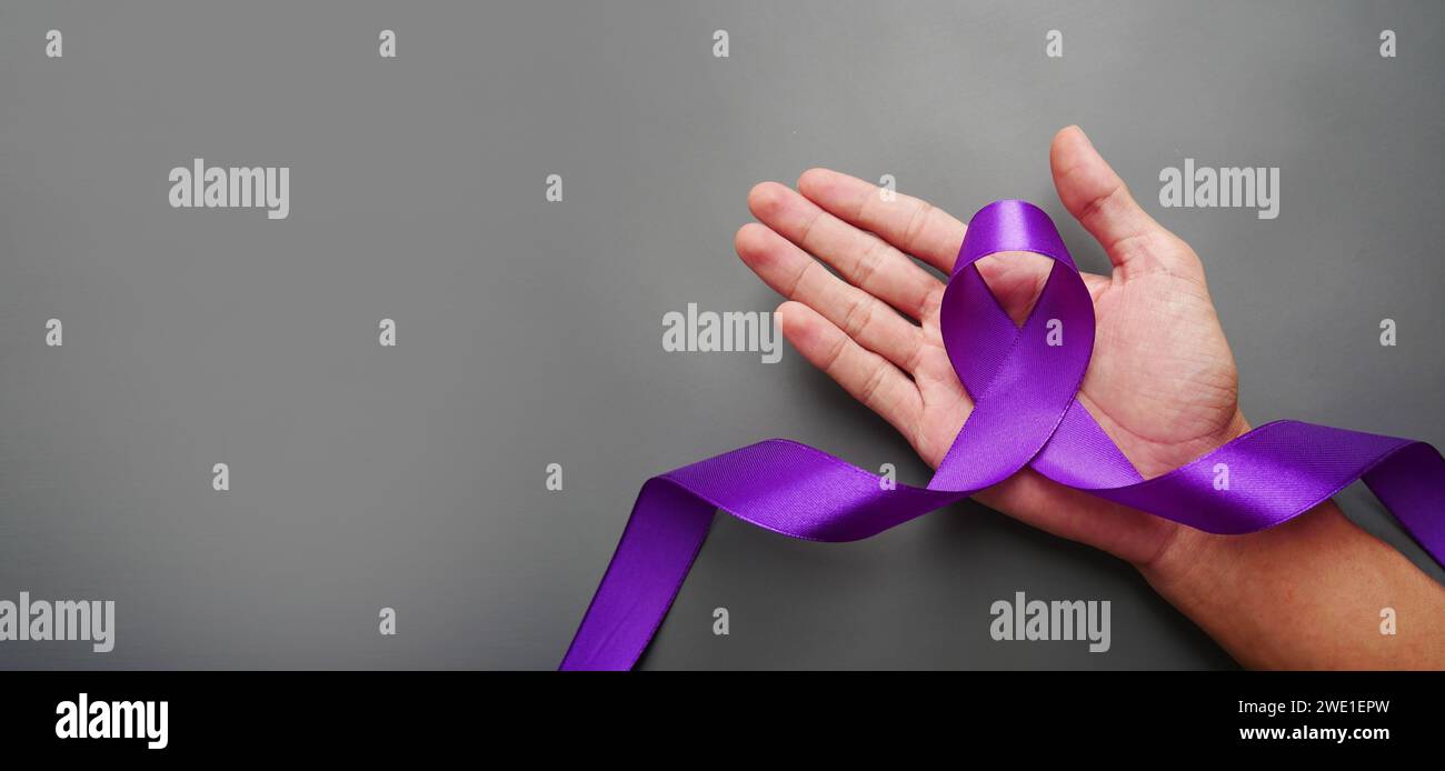Eine Hand, die ein luxuriöses lila Band auf grauem Hintergrund hält. Lila Schleife mit Pankreaskarzinom-Bewusstsein. Stockfoto