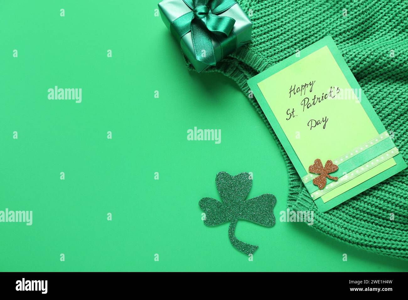 Karte mit Text HAPPY ST. PATRICK's DAY, Geschenkbox und Pullover auf grünem Hintergrund Stockfoto