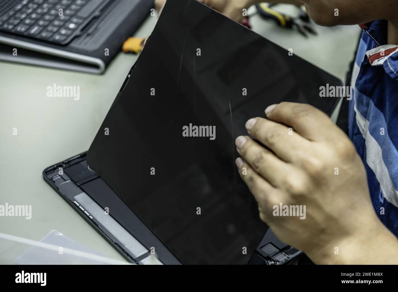 Ein Techniker in der elektronischen Werkstatt, der Teile auf einem Tablet-Bildschirm festschrauben kann Stockfoto