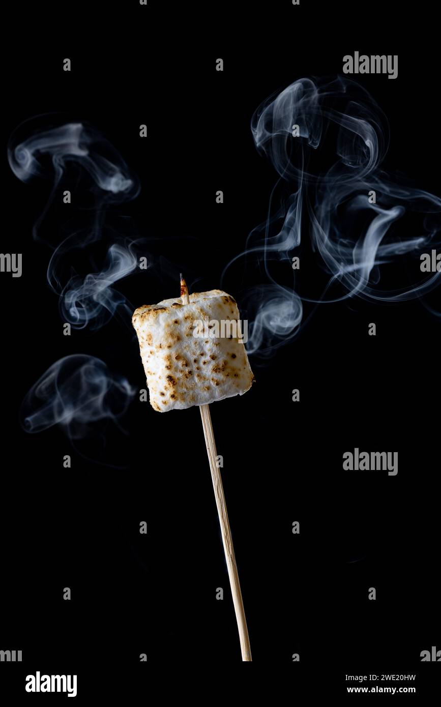 Nahaufnahme eines rauchenden und röstenden Marshmallow auf einem Stock isoliert auf schwarzem Hintergrund Stockfoto