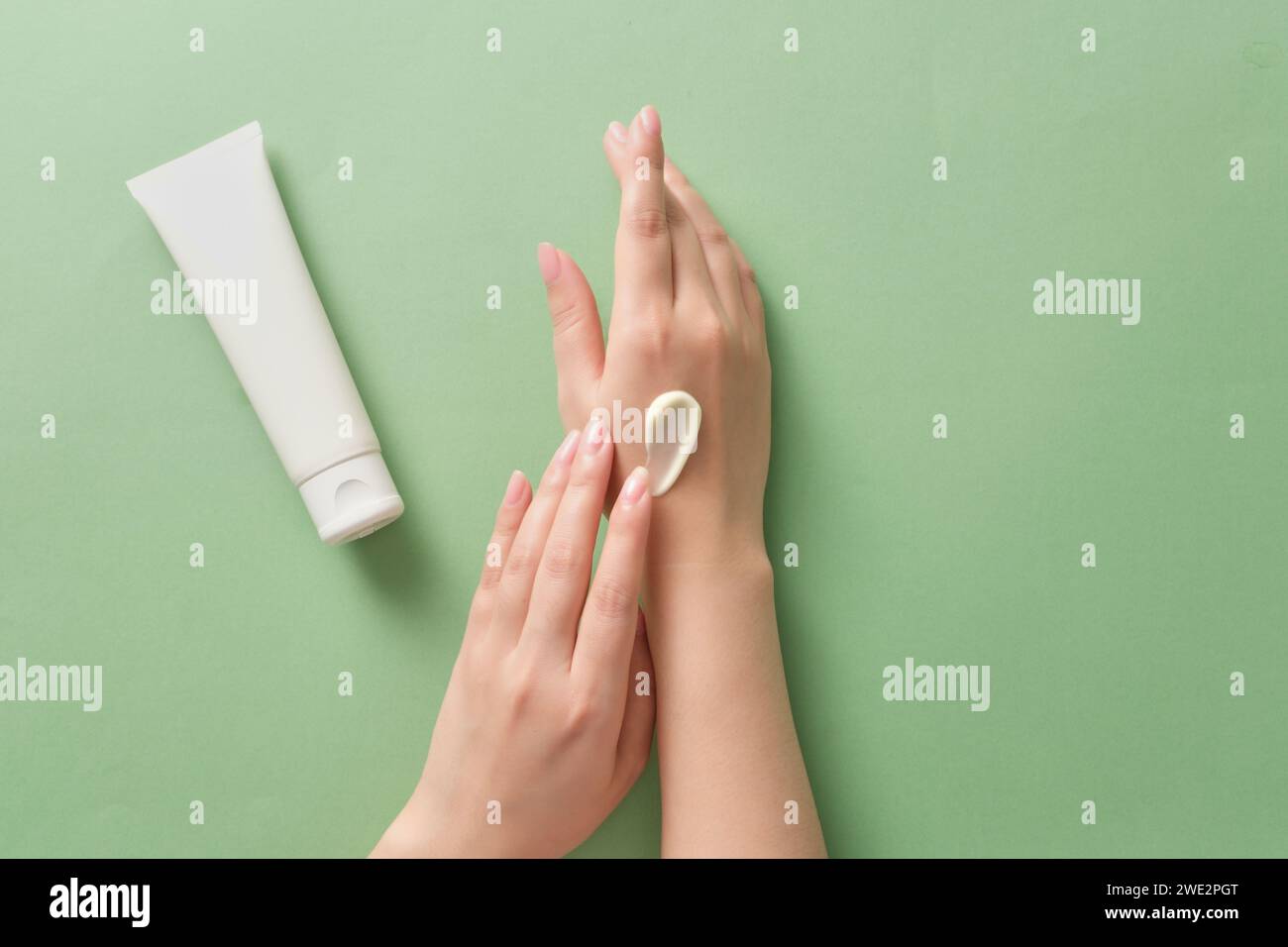 Schöne Frauenhand, die Creme auf der anderen Seite aufträgt, daneben ist eine leere weiße Kosmetikröhre ohne Marke für Design. Hautpflegekonzept, versuchen Sie Anti-Irri Stockfoto