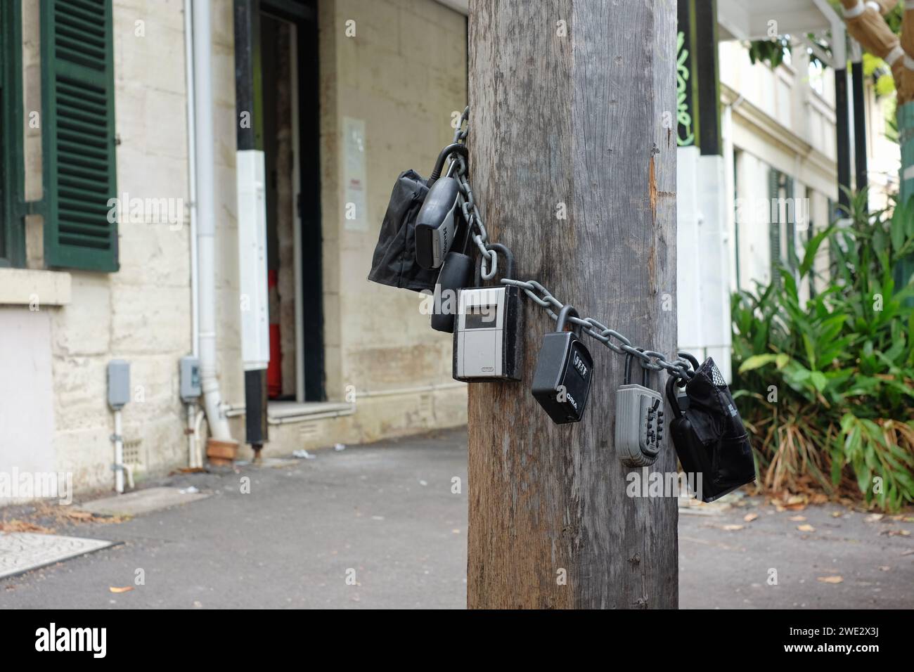 Sieben Kombinationsschlüssel-Schließfächer an einer Kette um einen hölzernen Lichtmast auf dem Fußweg für Airbnb Kurzzeitwohnungen in Sydney Stockfoto