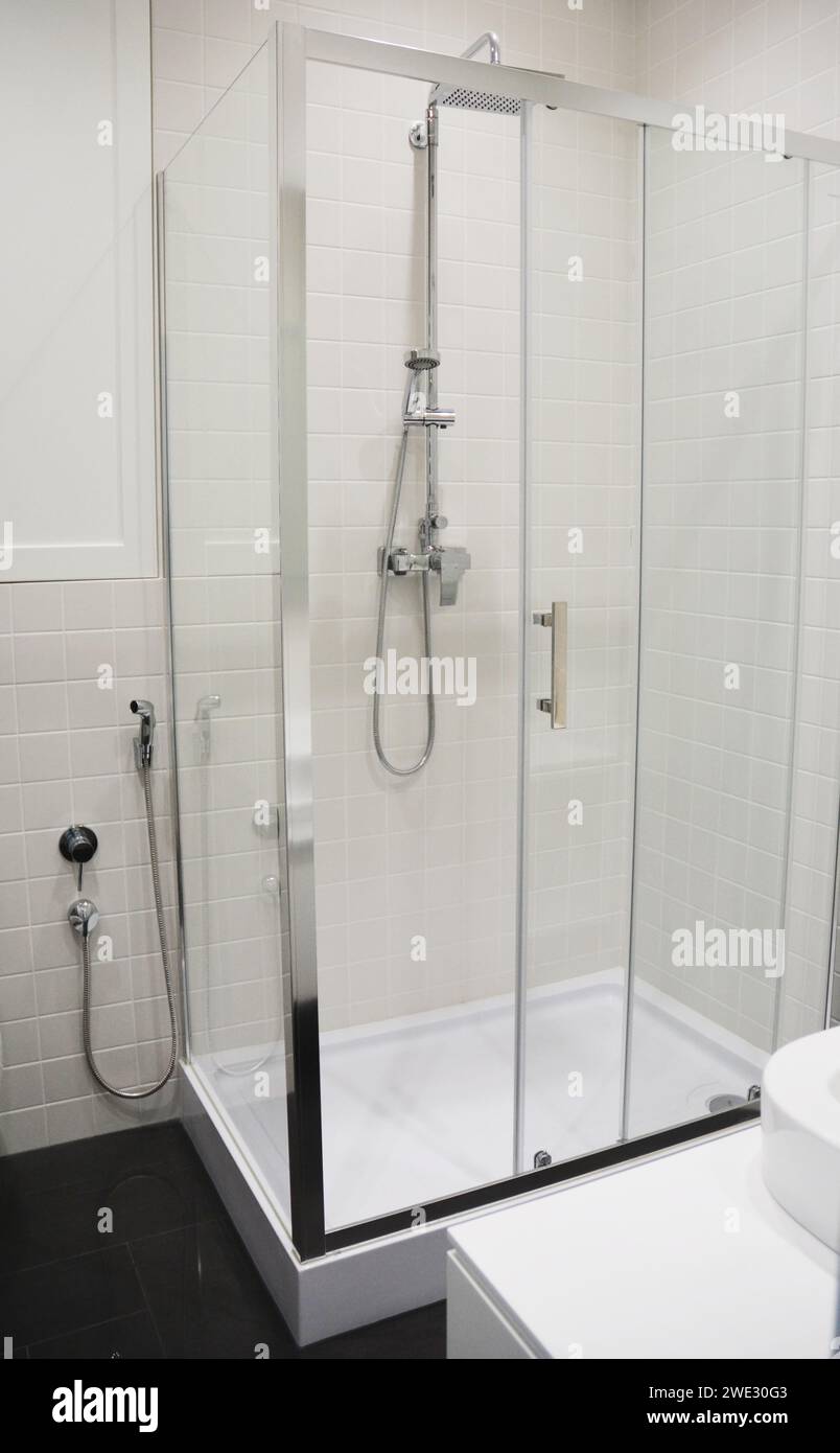 Eine Nahaufnahme einer modernen rechteckigen Duschkabine, einer Kabine mit Duschkopf und einer Bidet-Dusche in einem schwarz-weiß gefliesten Badezimmer. Stockfoto