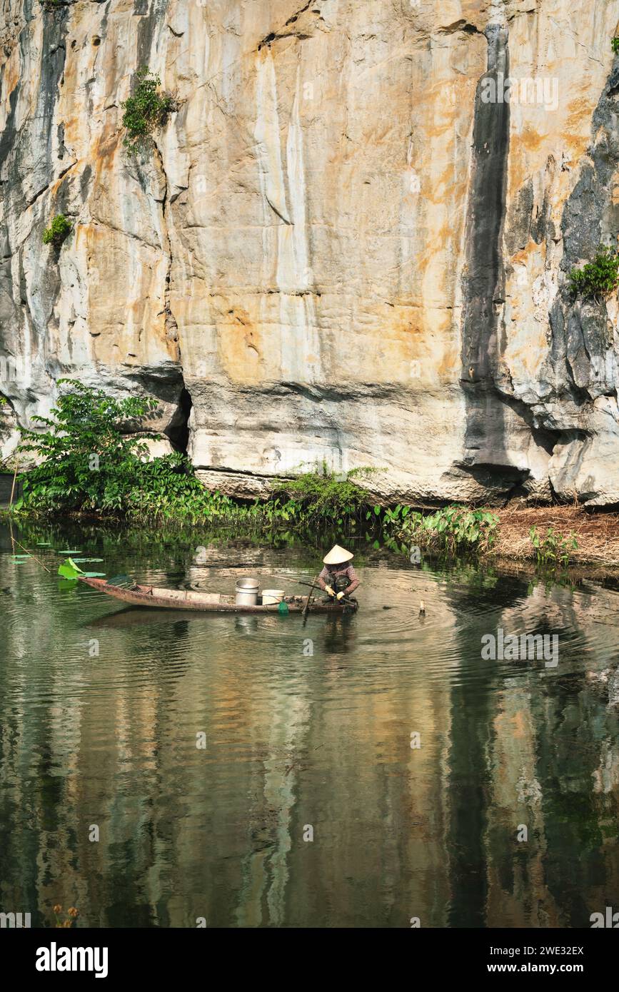 Vietnamesische Frau mit traditionellem Hutfischen auf einem Boot entlang der Kalksteinklippe in Ninh Binh, Vietnam Stockfoto