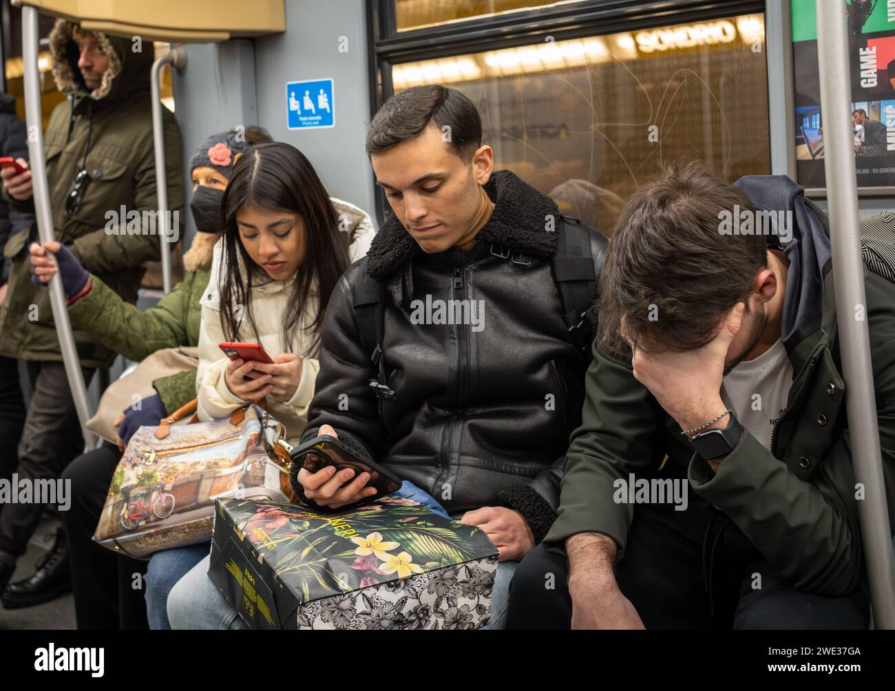 Passagiere schauen auf Mobiltelefone, während ein Mann in einer U-Bahn in Mailand, Italien, seinen Kopf in der Hand hält. Stockfoto