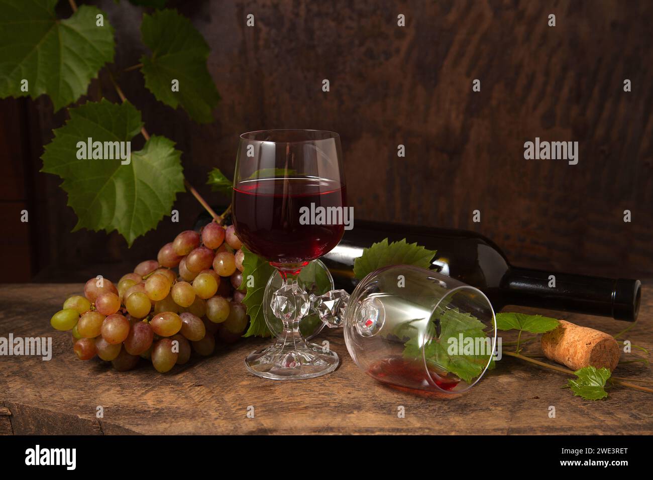 Das Konzept eines köstlichen alkoholischen Getränks, Wein und Trauben. Weinflasche, Trauben, leeres Glas und Glas Rotwein auf dunklem rustikalem holzbalkon Stockfoto