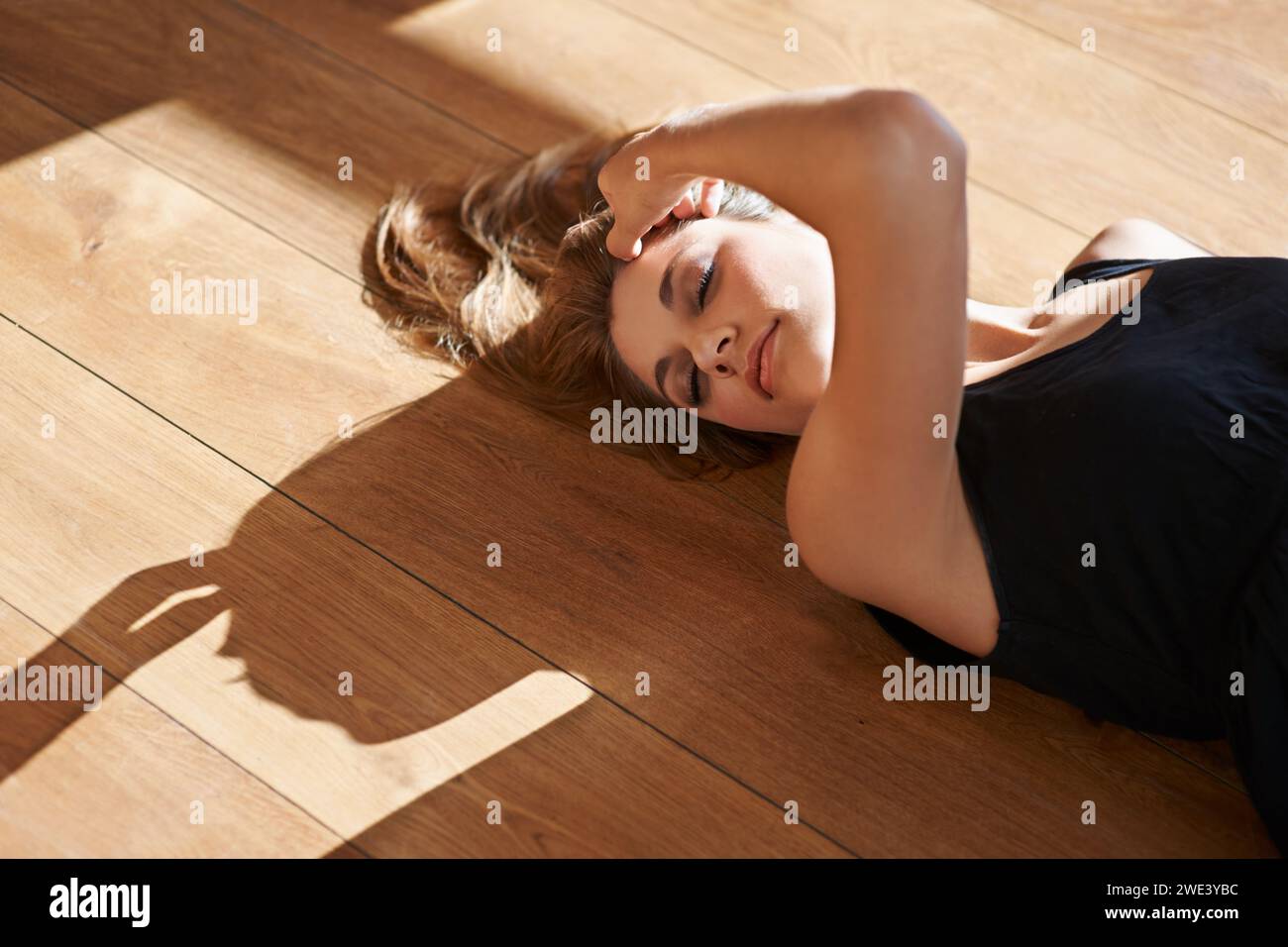 Haus, Holzboden und Frau in Sonnenschein mit Schönheit oder und Glanz auf Haut in der Schweiz Wohnung. Ruhig, Person und Mädchen liegen mit Schatten auf dem Boden Stockfoto