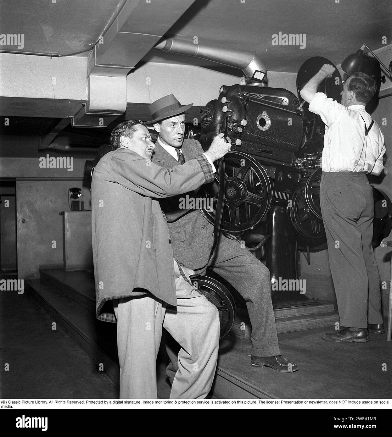 Hasse Ekman. 1915-2004. Schwedischer Schauspieler und Regisseur. Hier mit dem Filmproduzenten Lorens Marmstedt. 1908-1966 in einem Kinovorstellungsraum. Sie stehen im Projektorraum eines Kinos und schauen sich den Filmstreifen einer Filmrolle genau an, der im Projektor gezeigt werden soll. 1952. Kristoffersson Ref. BG91-4 Stockfoto